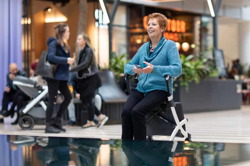 A senior woman enjoying her tea break on a walker chair in a lively shopping mall.